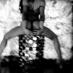 A woman seated on a mirrored column, dressed in fishnets.